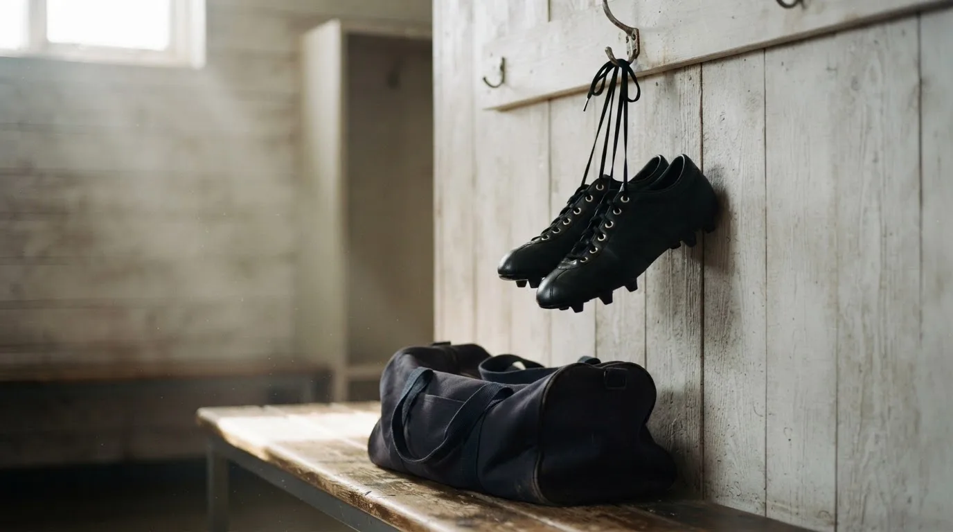 Ein Paar Fussballschuhe hängt an einem Haken in einer ruhigen Umkleide, darunter steht eine Sporttasche auf einer Holzbank.
