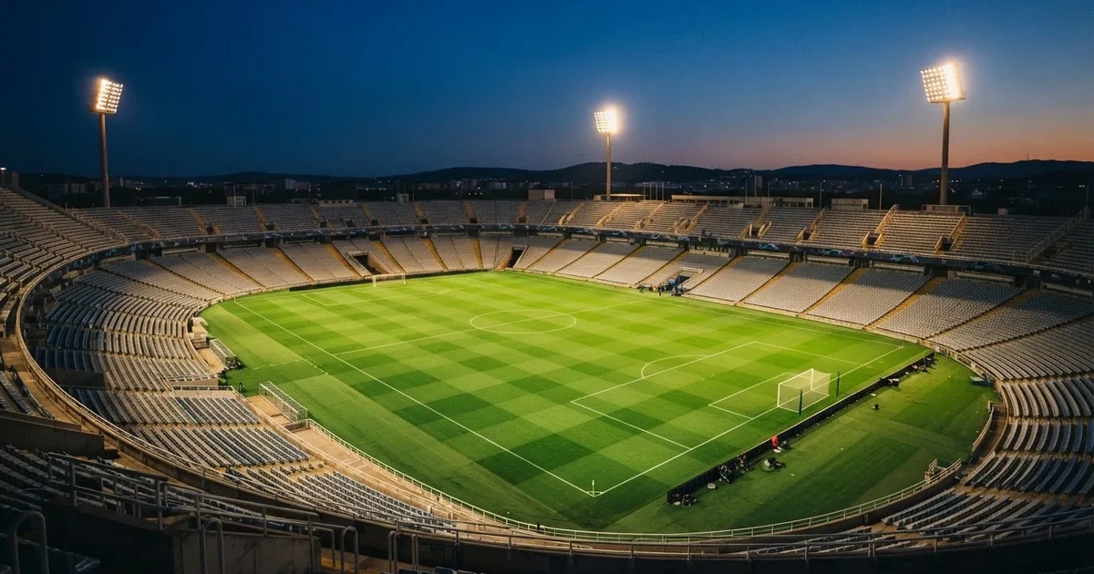 Ein Fussballstadion bei Flutlicht von einer Anhöhe aus gesehen, der Rasen leuchtet grün unter dunklem Abendhimmel
